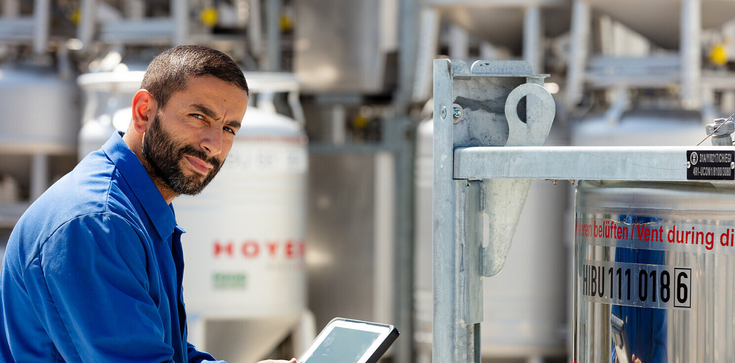 Employee stands in front of an IBC tote and holds a tablet in his hand