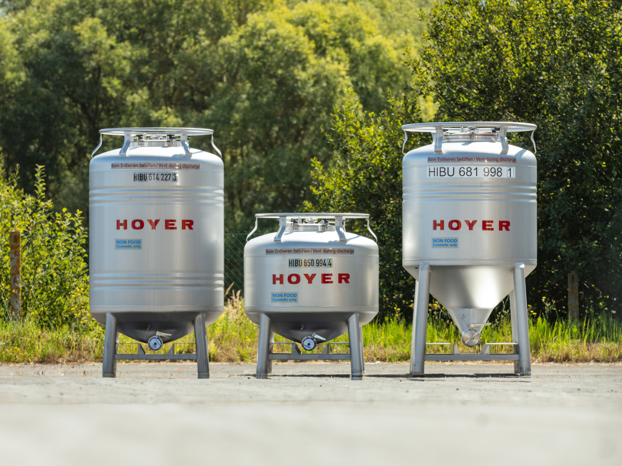 Three HOYER Group IBC totes with green bushes in the background