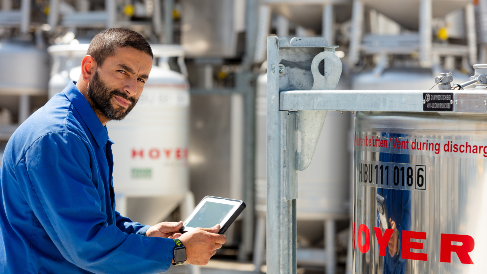 Employee stands in front of an IBC tote and holds a tablet in his hand